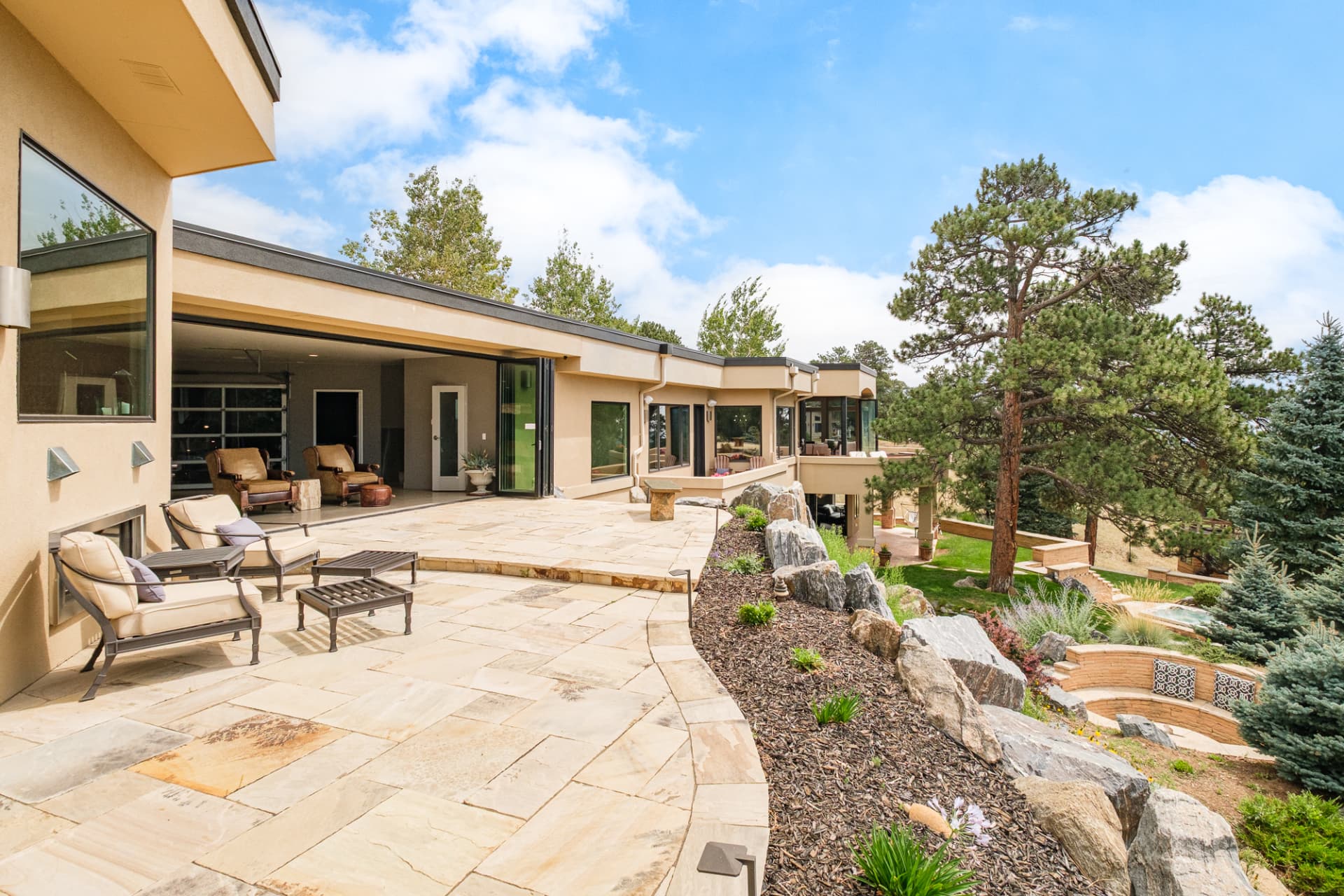 Flagstone terrace with lounge seating, folding glass walls, and pines beyond