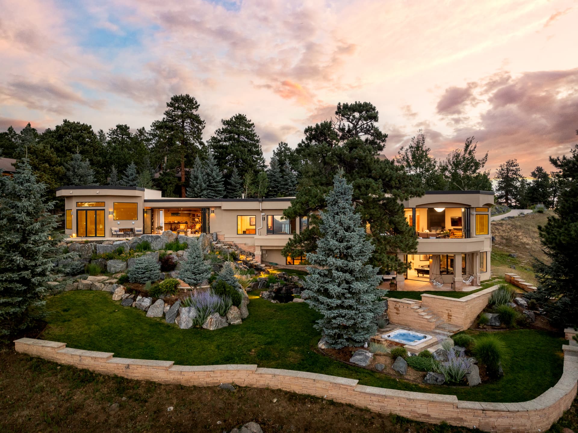 Dusk aerial of the residence with warm interior light and mountain backdrop